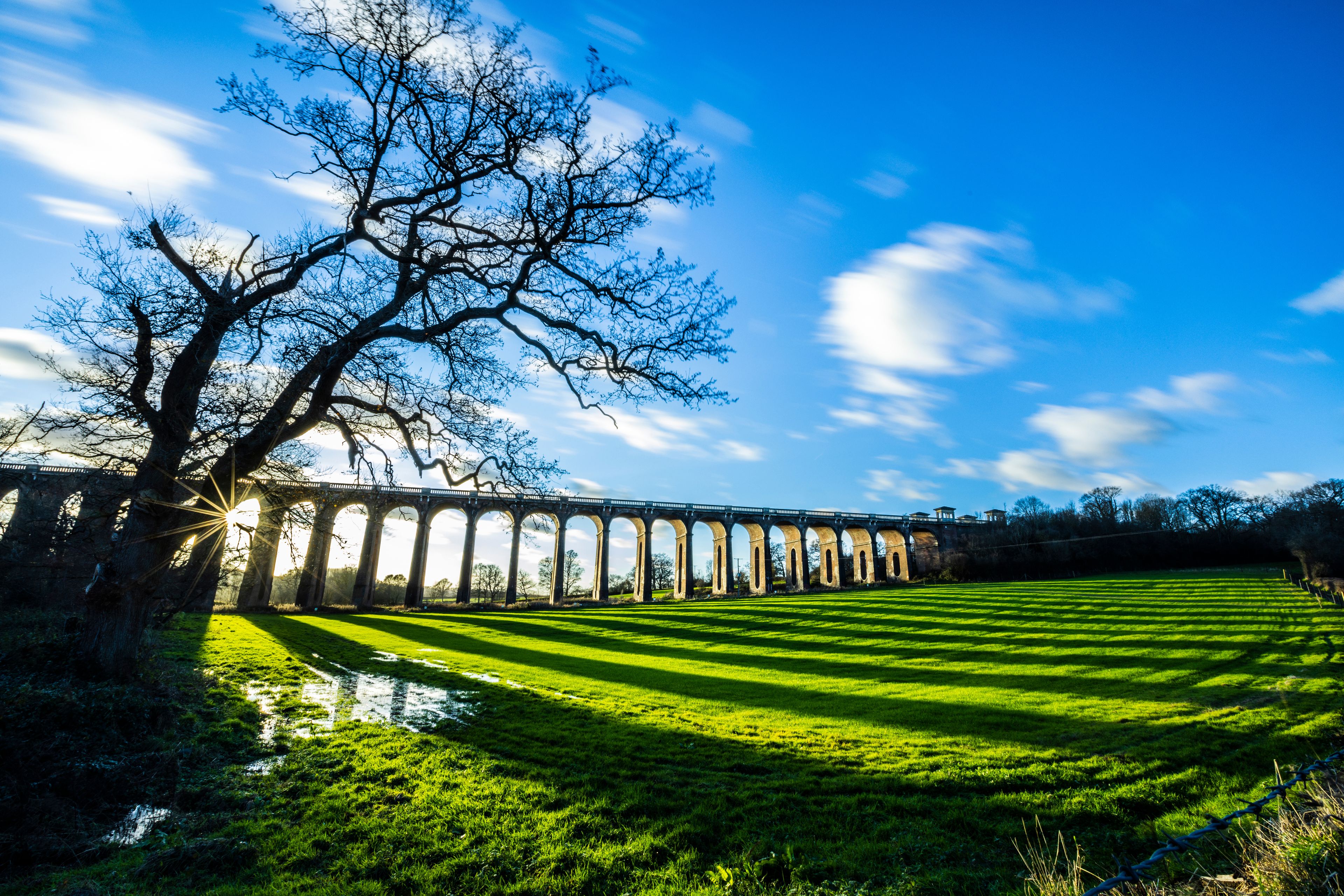 The Ouse Valley Viaduct on an autumn afternoon with clouds streaming overhead and long shadows across the field.