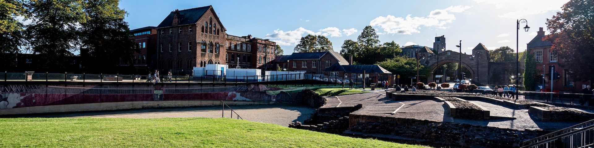 Un parque con un césped, un puente y edificios históricos al fondo.