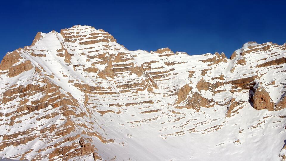 A snow-covered mountain with distinct horizontal layers and a clear blue sky.