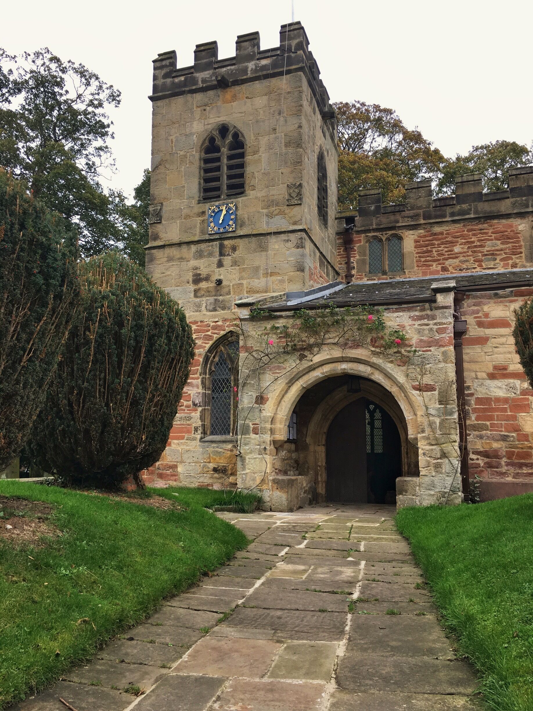 A historic stone building with a clock tower, arched entrance, and a pathway leading to it.