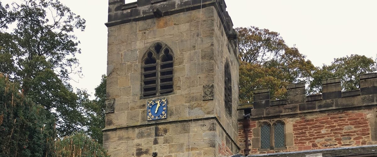 A historic stone building with a clock tower, arched entrance, and a pathway leading to it.