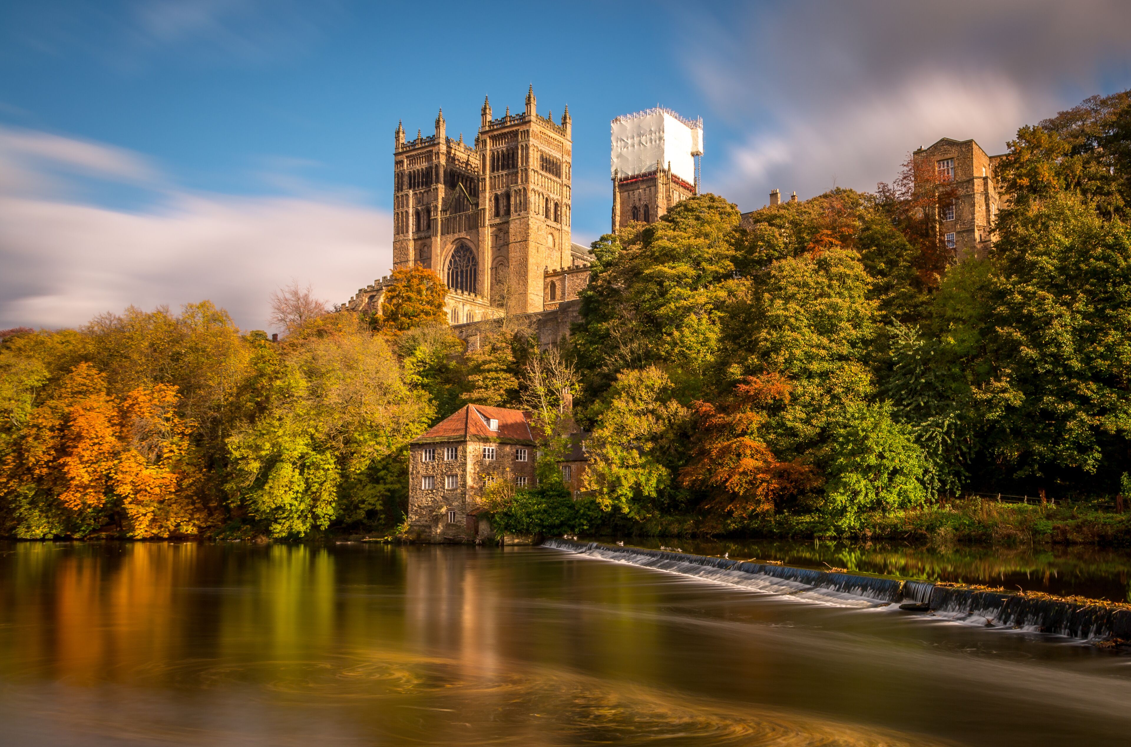 A historic cathedral, a stone building, and a river with a waterfall.