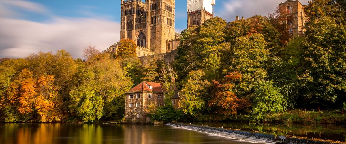 A historic cathedral, a stone building, and a river with a waterfall.