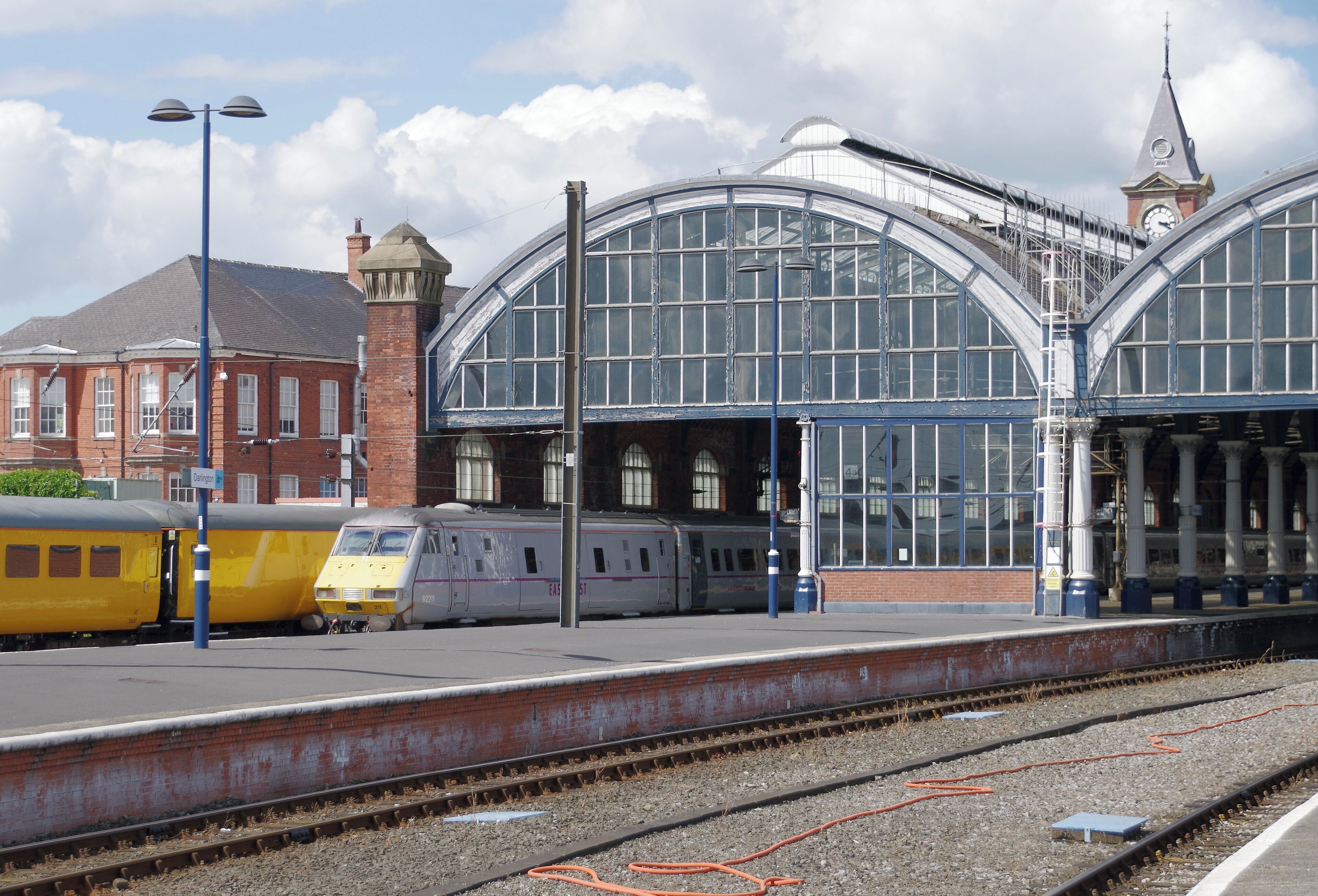 A train station with a large glass roof, a clock tower, and a historic building in the background.