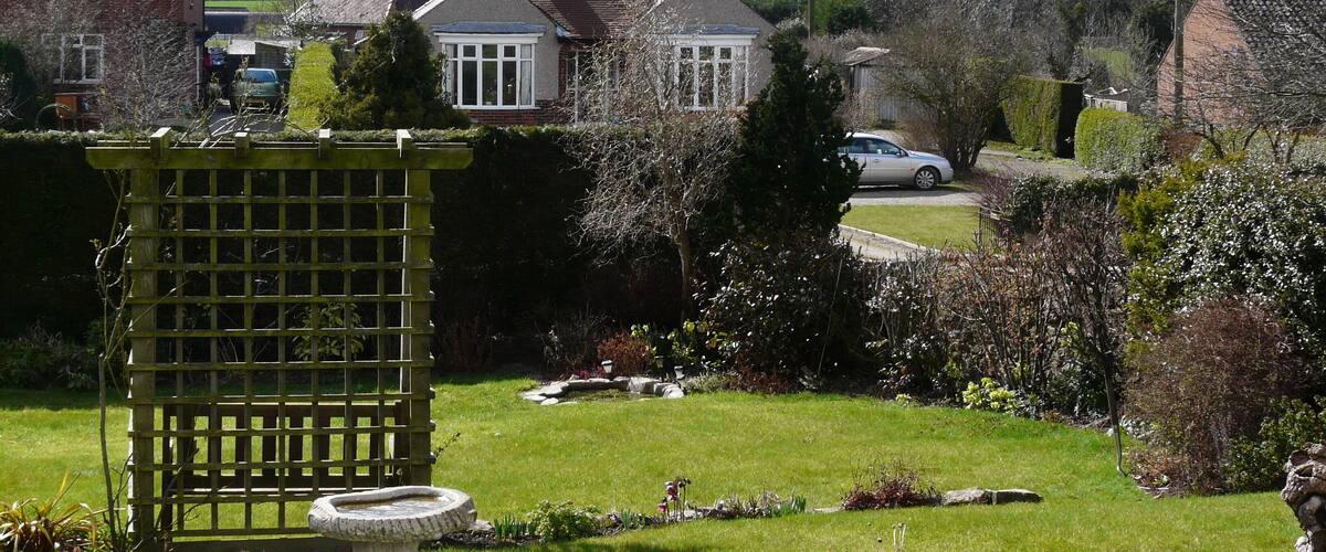 A residential area with houses, a garden, and a white car parked on the street.