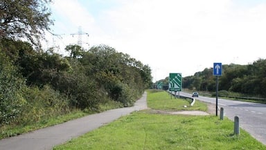 Um caminho ao lado de uma estrada, com uma placa de sinalização e uma seta azul.