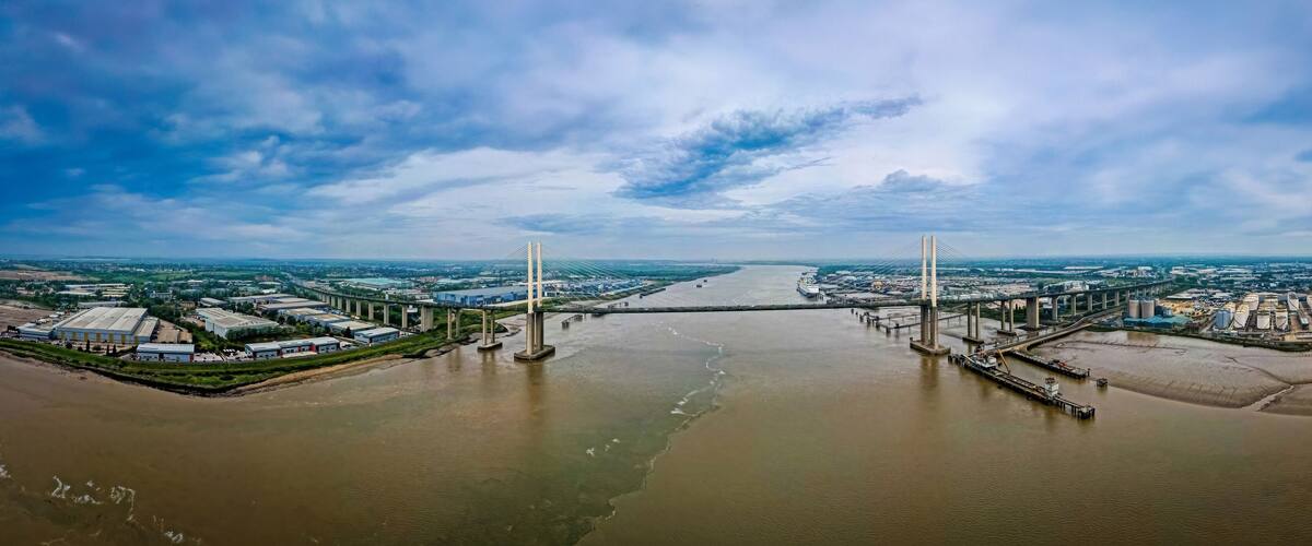 A large river with a bridge spanning across it, surrounded by industrial buildings and warehouses.