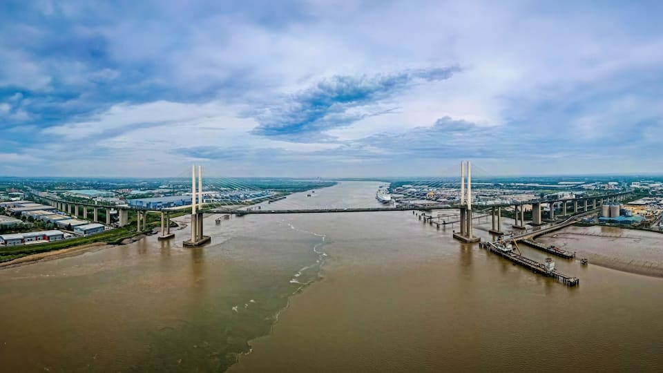 Un río caudaloso con un puente que lo atraviesa, rodeado de edificios industriales y almacenes.