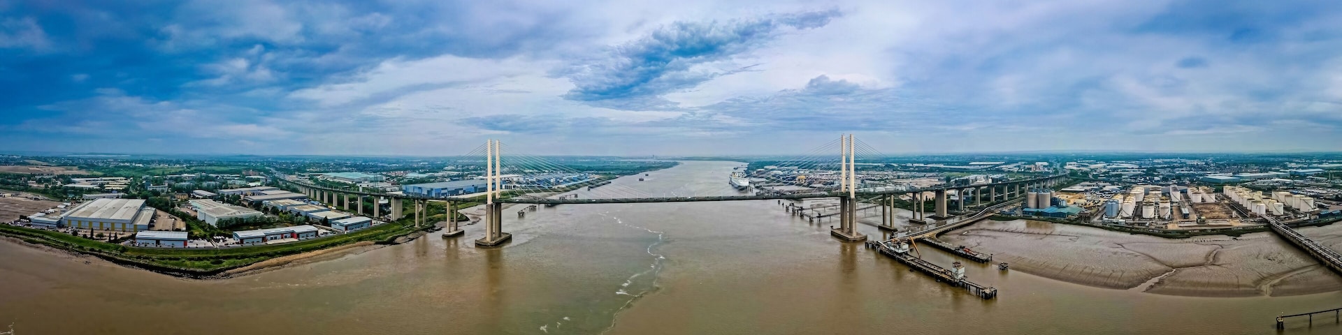 Un río caudaloso con un puente que lo atraviesa, rodeado de edificios industriales y almacenes.