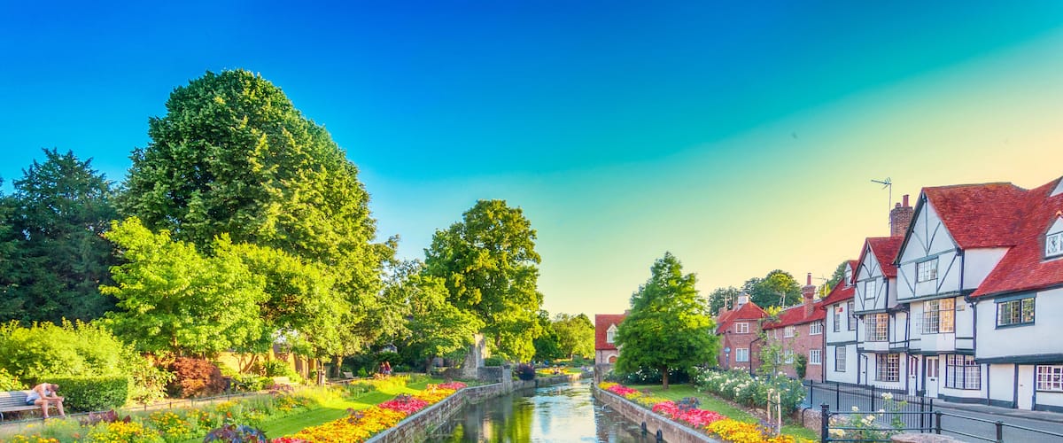 A canal with colorful flower beds, trees, and traditional buildings along the banks.