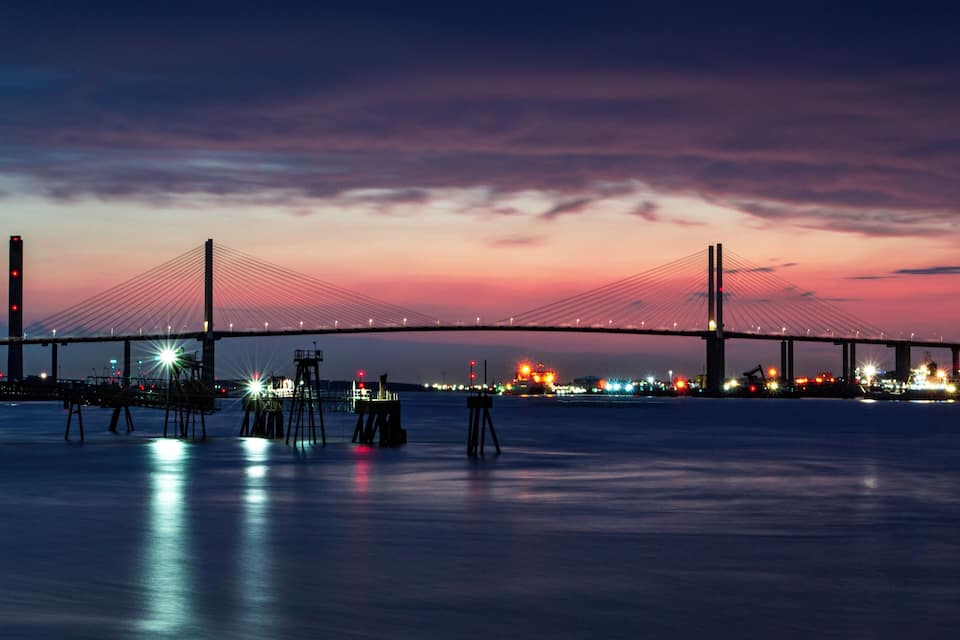 A bridge at dusk with lights reflecting on the water.