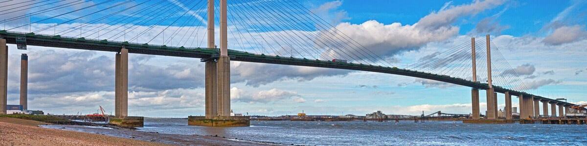 Eine große Hängebrücke über einem Fluss mit einem Kiesstrand im Vordergrund.