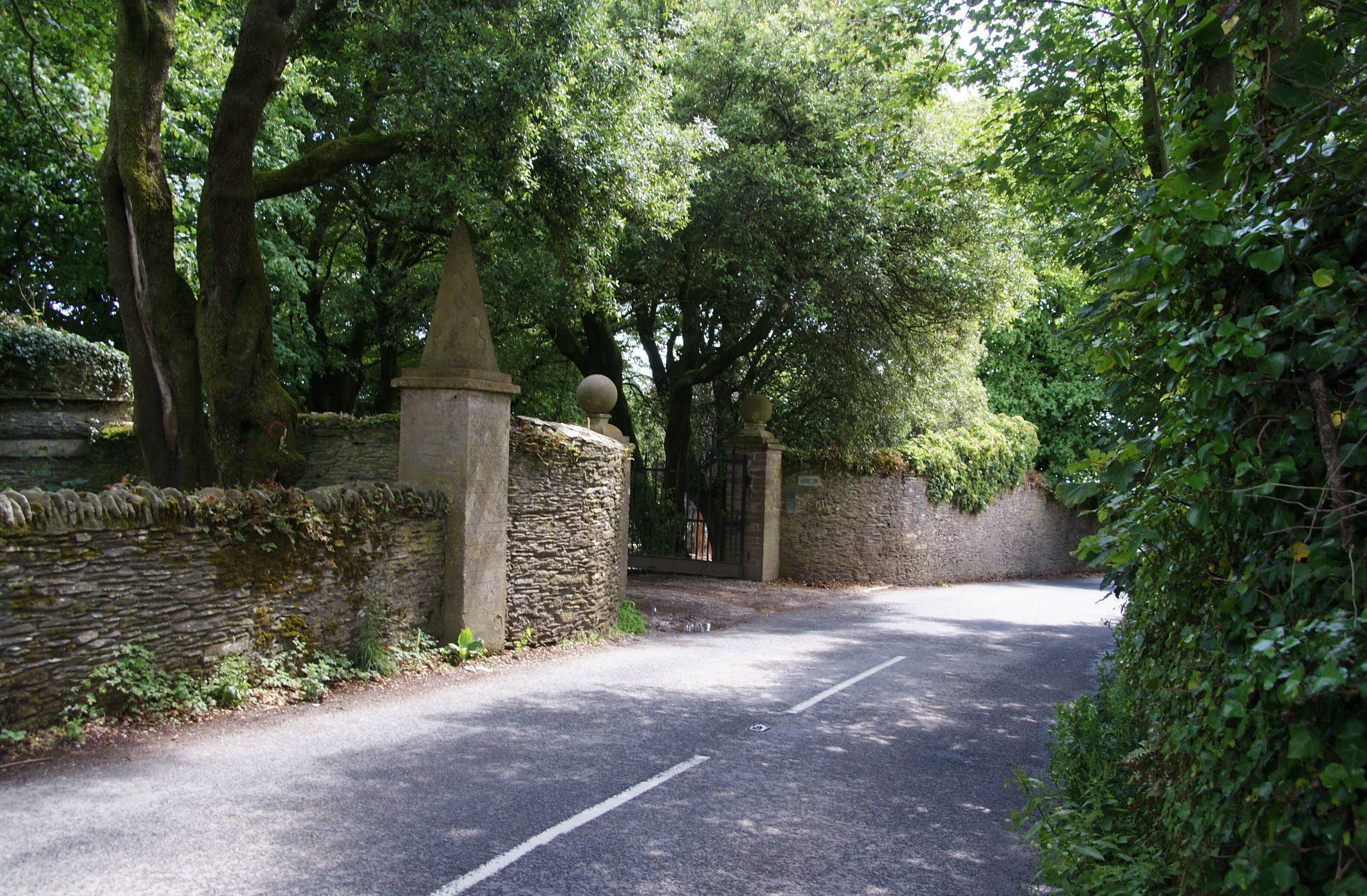 A narrow road flanked by stone walls and lush greenery.