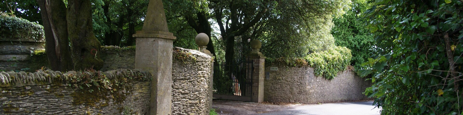 A narrow road flanked by stone walls and lush greenery.