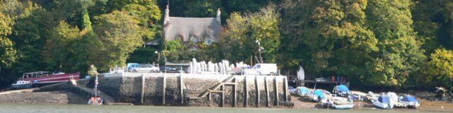 A dock with boats, a stone building, and a forested hillside.