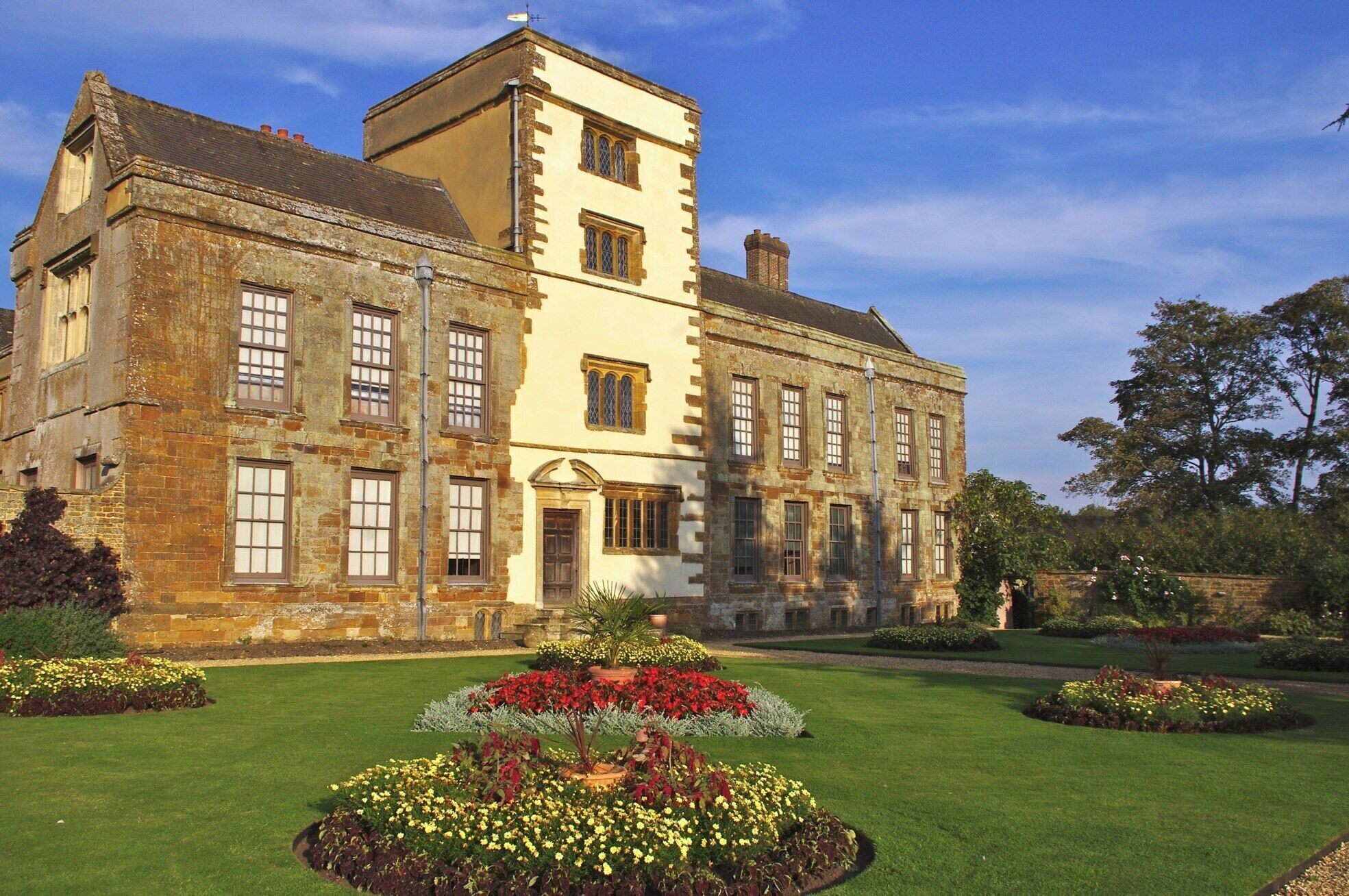 A historic building with a tower, large windows, and a well-maintained garden with various flowers.