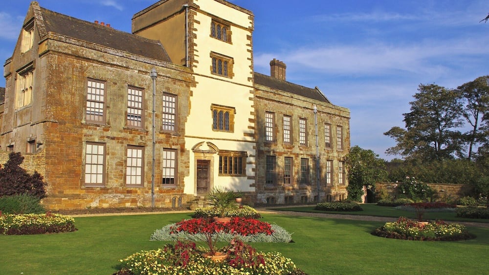 A historic building with a tower, large windows, and a well-maintained garden with various flowers.