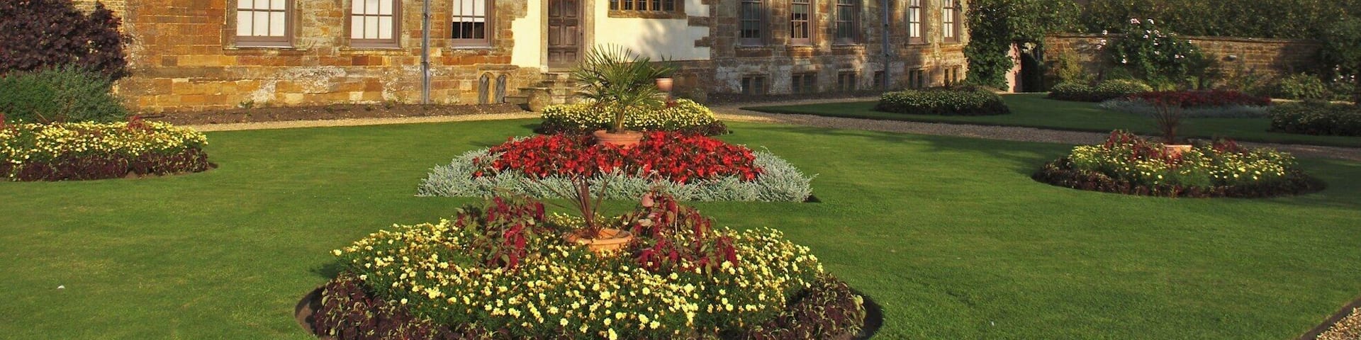 A historic building with a tower, large windows, and a well-maintained garden with various flowers.