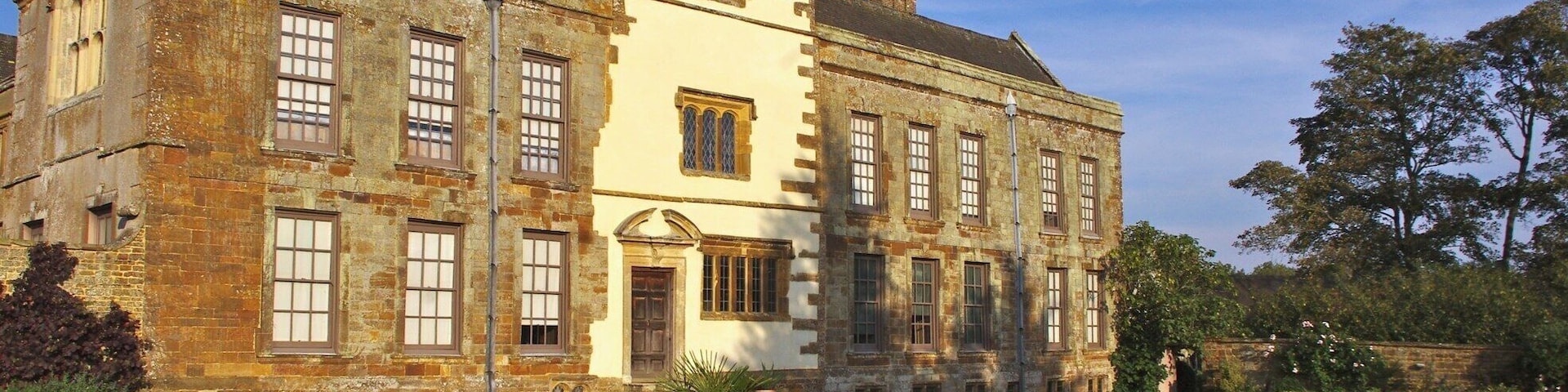 Um edifício histórico com uma torre, grandes janelas e um jardim bem cuidado com diversas flores.