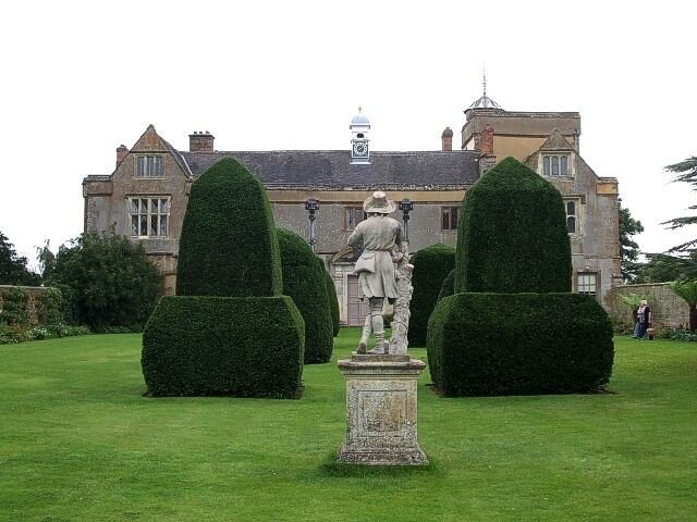 A statue in a garden with a large building in the background.