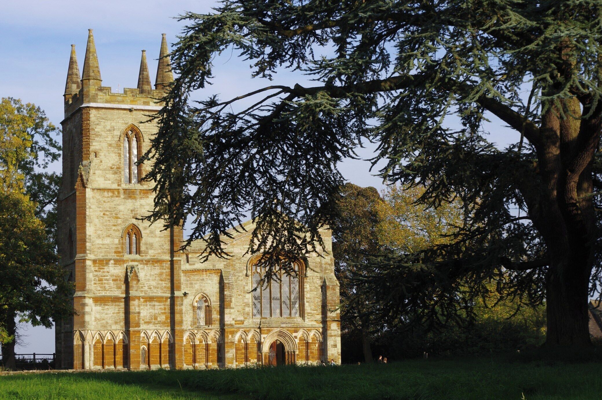 A historic stone church with pointed arches and a large tree in the foreground.
