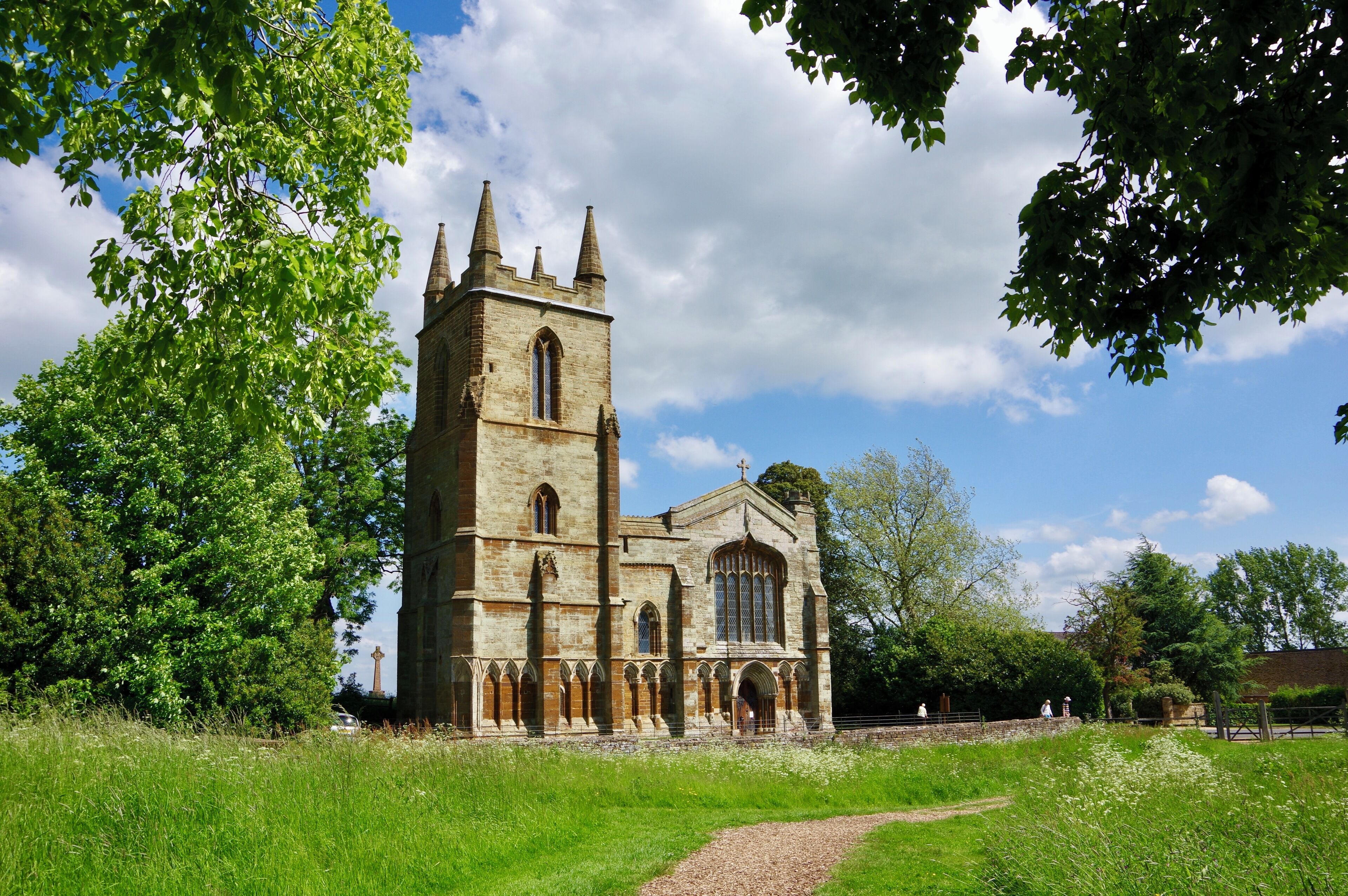 A historic church with a tall tower and arched windows, surrounded by lush greenery and a clear sky.