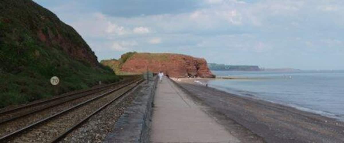 A coastal railway track leading to a beach with cliffs and a clear sky.