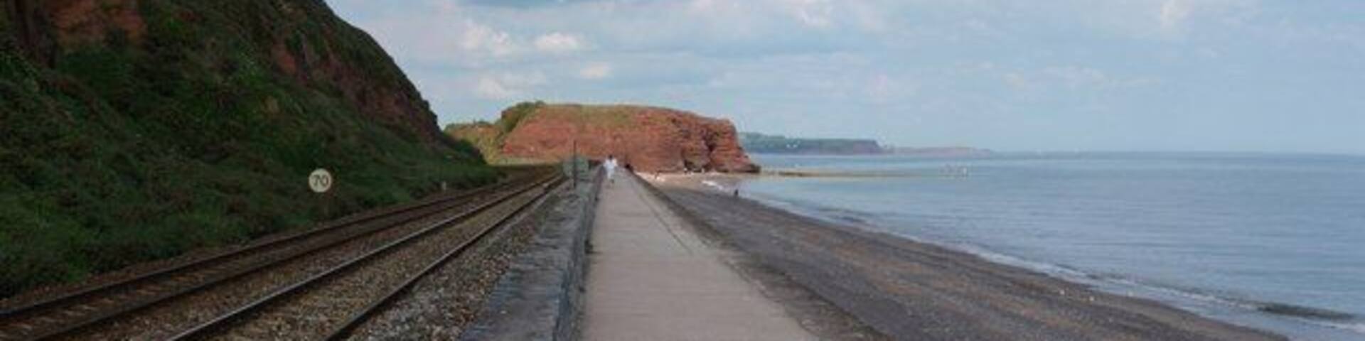A coastal railway track leading to a beach with cliffs and a clear sky.