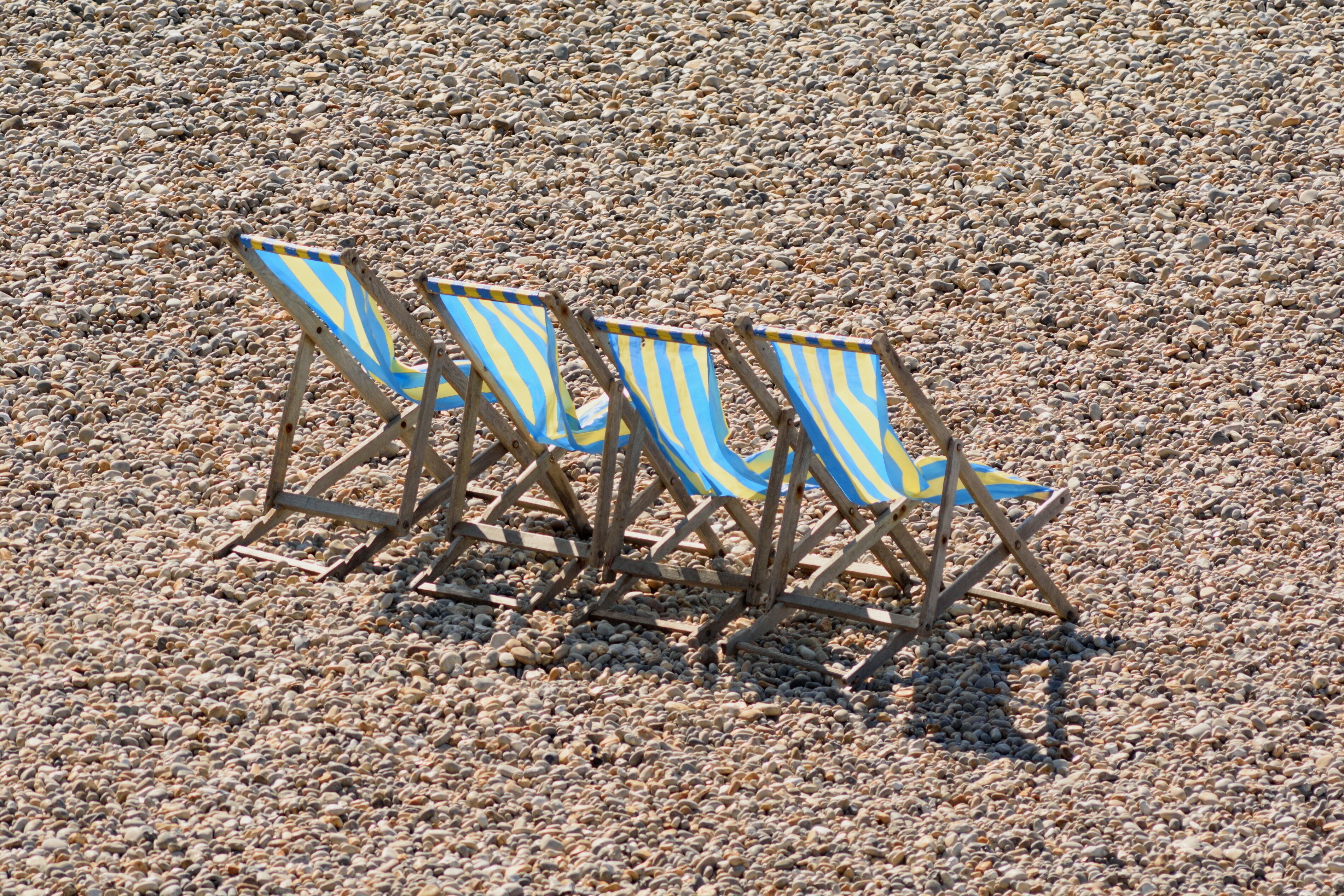 Three beach chairs with striped blue and yellow fabric on a pebbly beach.