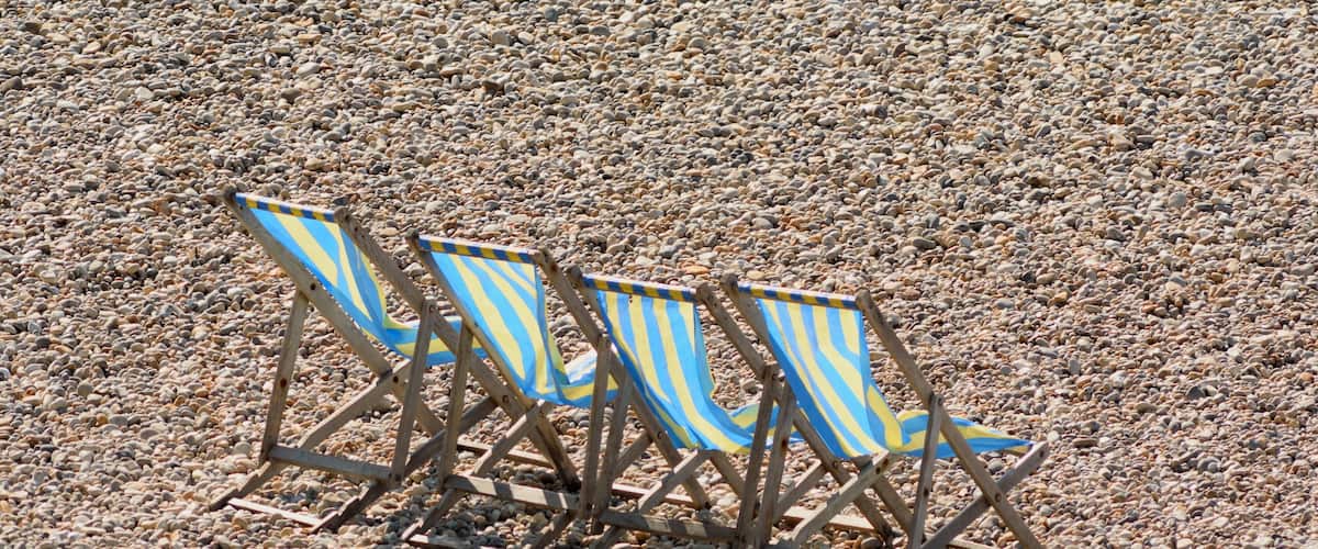 Three beach chairs with striped blue and yellow fabric on a pebbly beach.