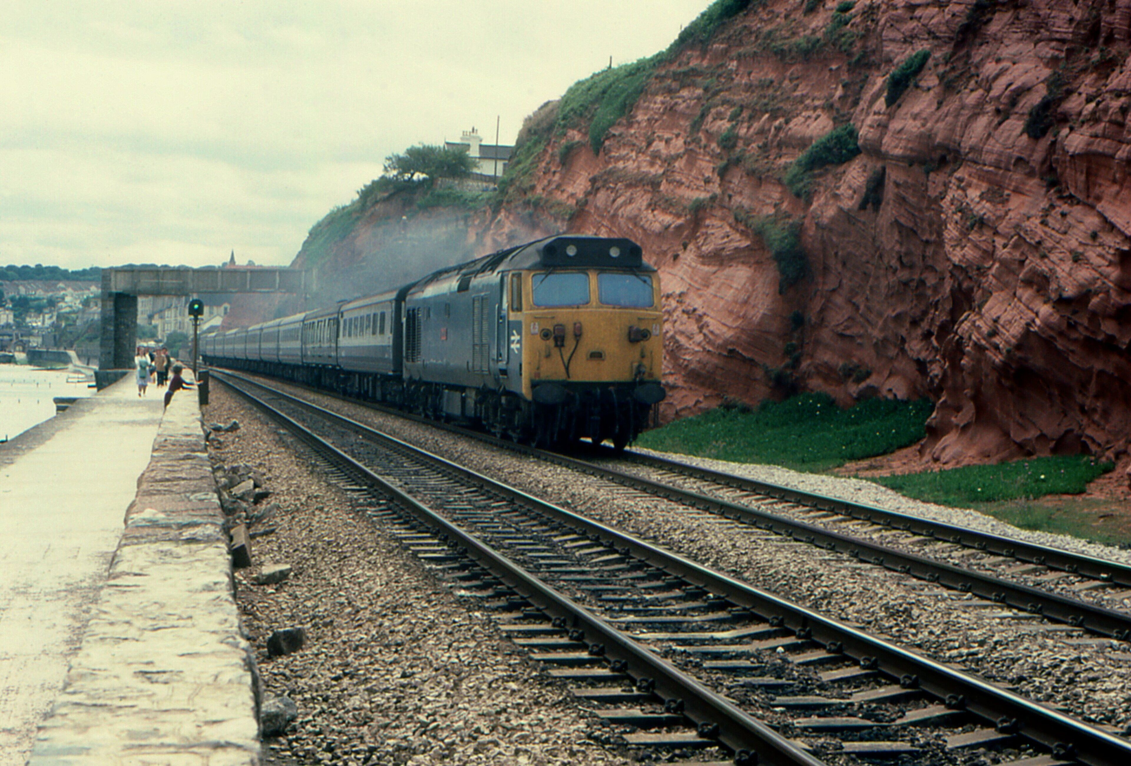 A train on tracks next to a cliff and a bridge.