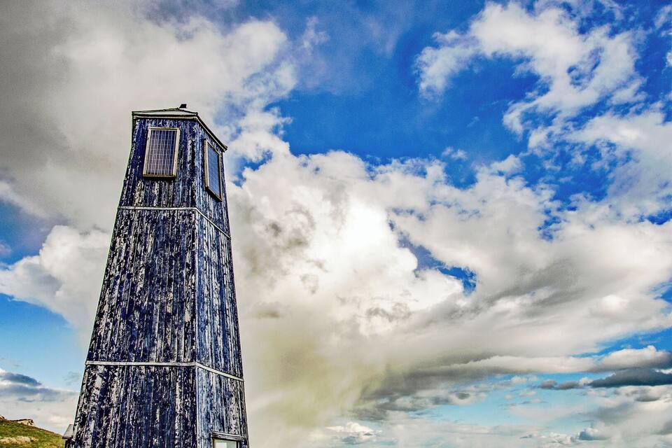 Een verweerde toren aan de zee, met een heldere lucht en een grasveld op de voorgrond.