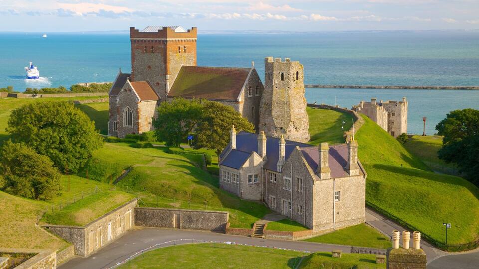 A historic castle with a tower, surrounded by lush green hills and a body of water.