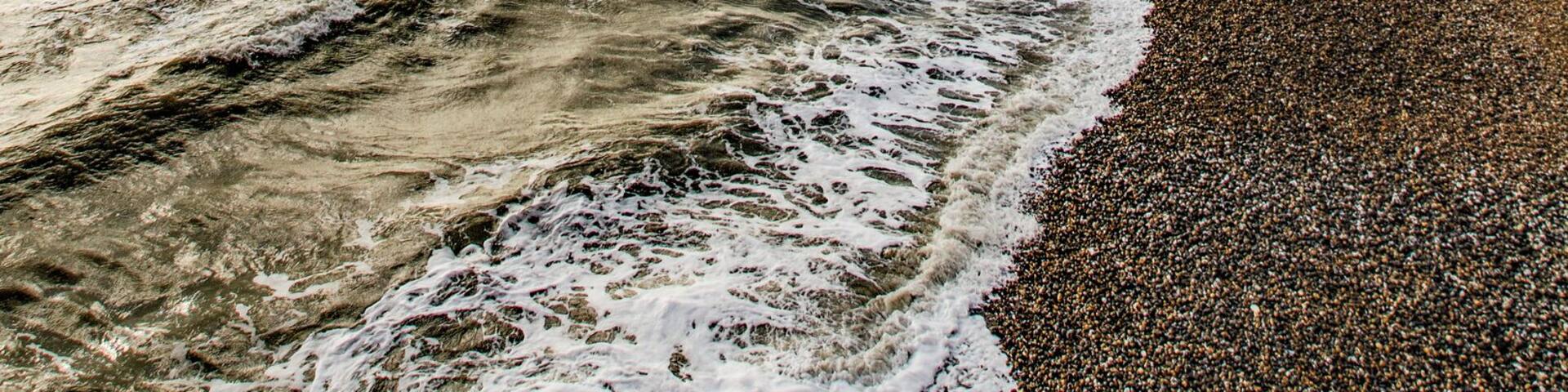A beach with waves, a rocky cliff, and a partly cloudy sky.