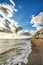 A beach with waves, a rocky cliff, and a partly cloudy sky.