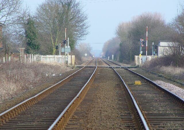 Railway tracks with a level crossing, wooden fence, and trees in the background.