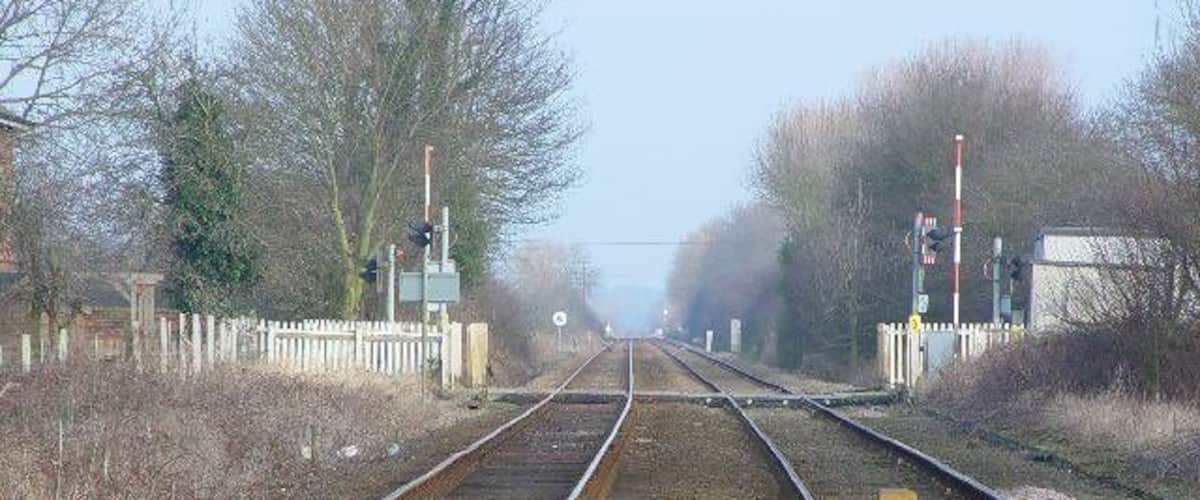 Railway tracks with a level crossing, wooden fence, and trees in the background.