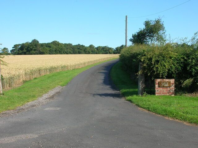 A rural road curving through a field with a stone marker on the right.