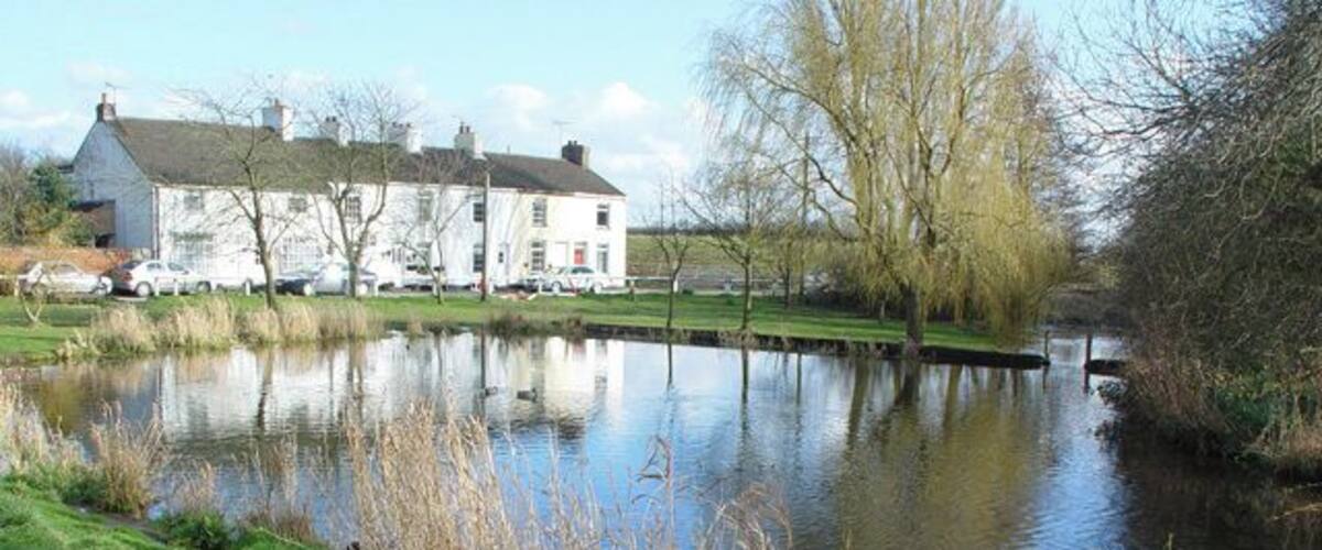 A calm river with a house and parked cars in the background.