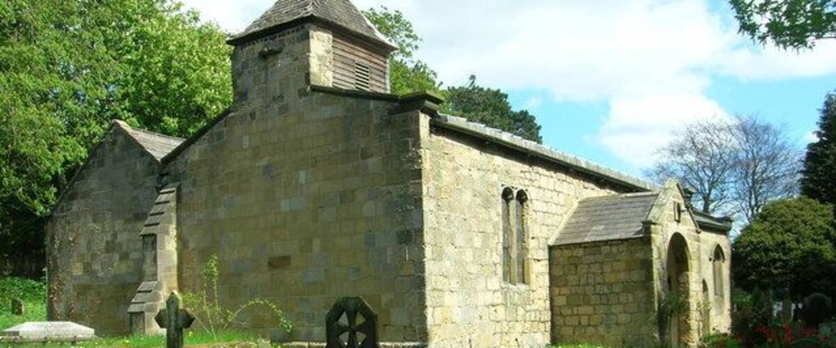 A stone church with a bell tower, surrounded by a cemetery with headstones.