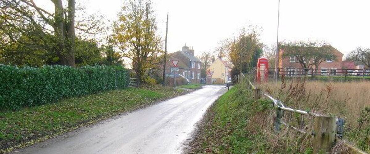 A narrow rural road with a hedge on one side and a red telephone box on the other.