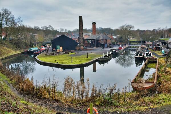 A canal with boats, a small dock, and industrial buildings.