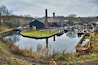 A canal with boats, a small dock, and industrial buildings.