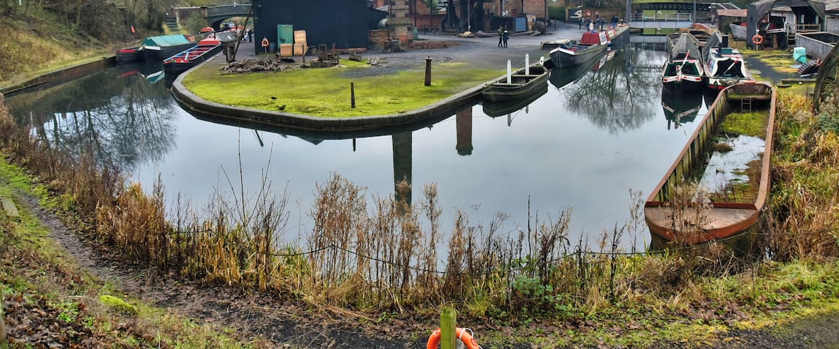 A canal with boats, a small dock, and industrial buildings.