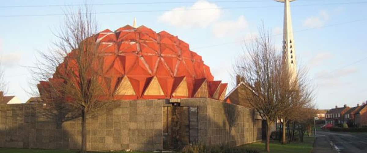 A large red geodesic dome building with a tall white spire in the background.