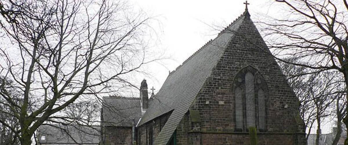 A church with a pointed roof and a cross on top, surrounded by gravestones in a cemetery.