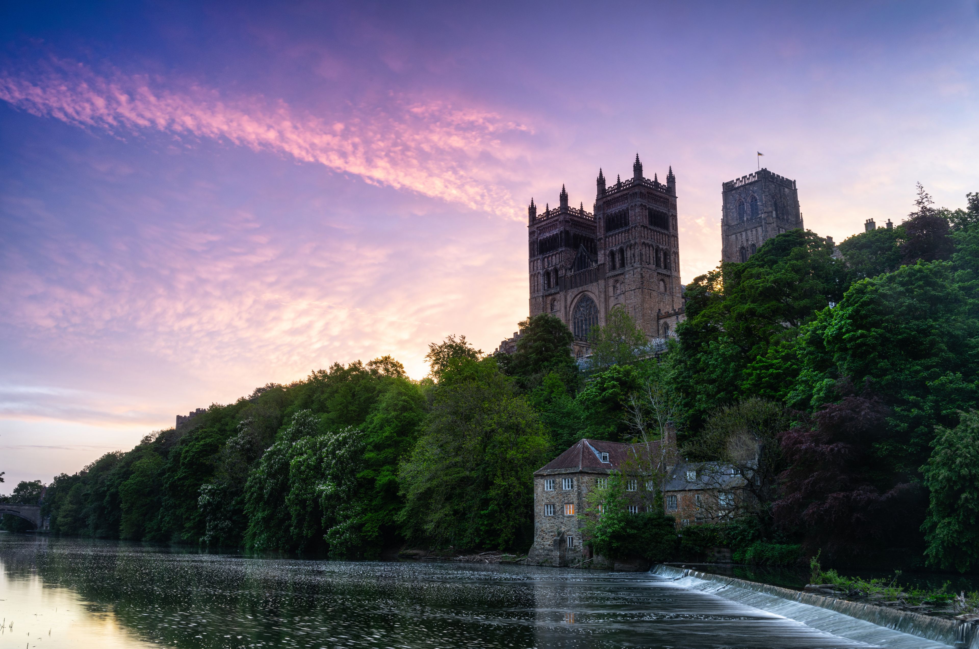 A castle with two towers, a river, and lush greenery.