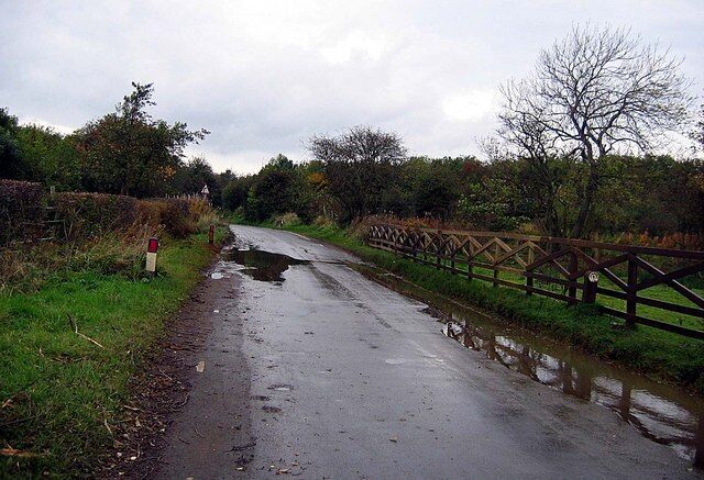 A rural road with puddles, a wooden fence, and a red post.