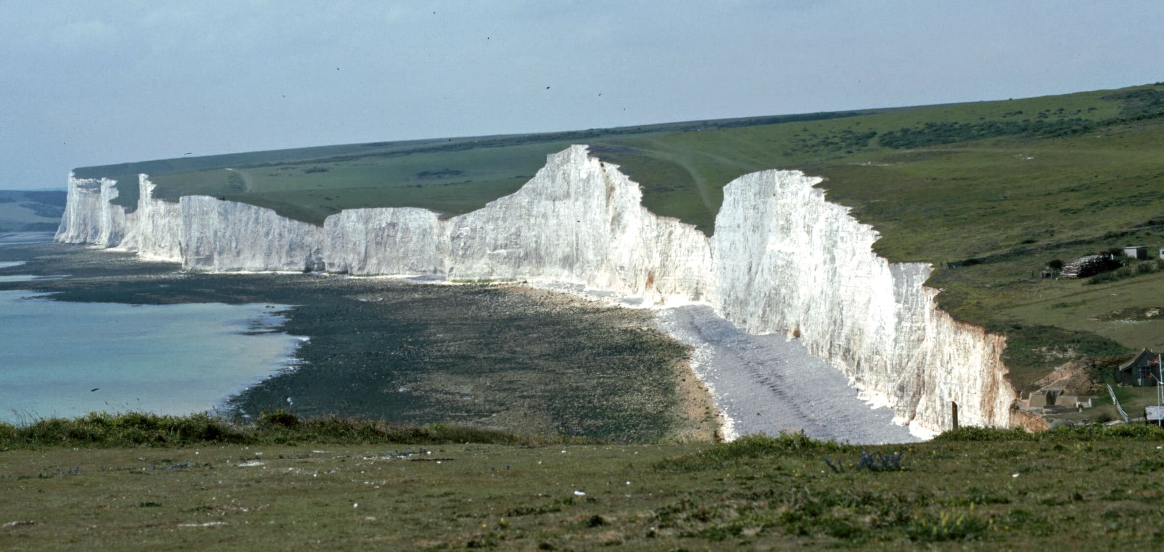 White cliffs along a coastline with a grassy hill in the background.