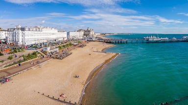 Paisagem costeira com uma praia arenosa, um píer que se estende para o mar e edifícios históricos ao longo da costa.